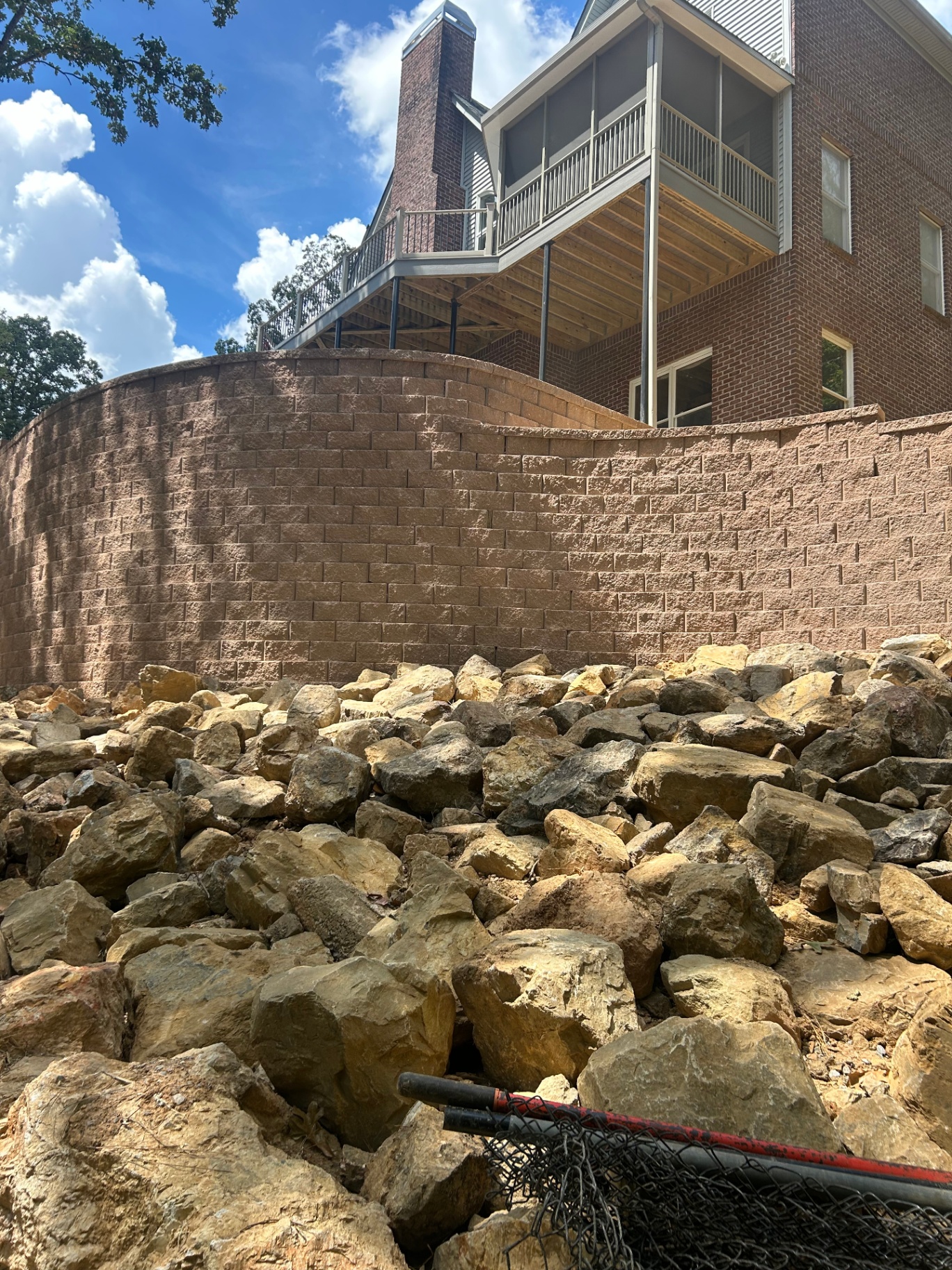 Tall curved retaining wall with boulder drainage below a deck