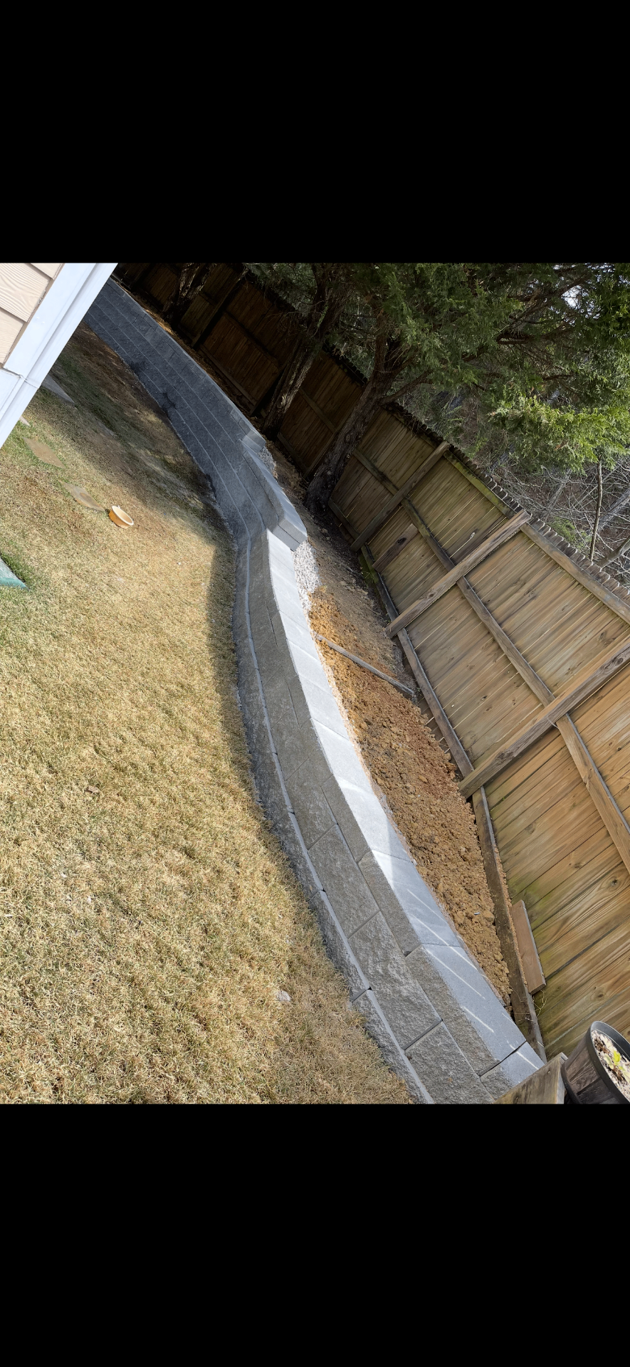 Long curved retaining wall along a backyard fence line